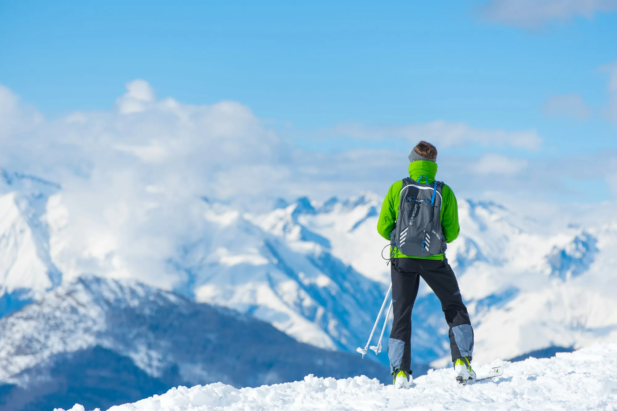 Ein Skitourengeher in grüner Jacke auf einem Gipfel über den Wolken